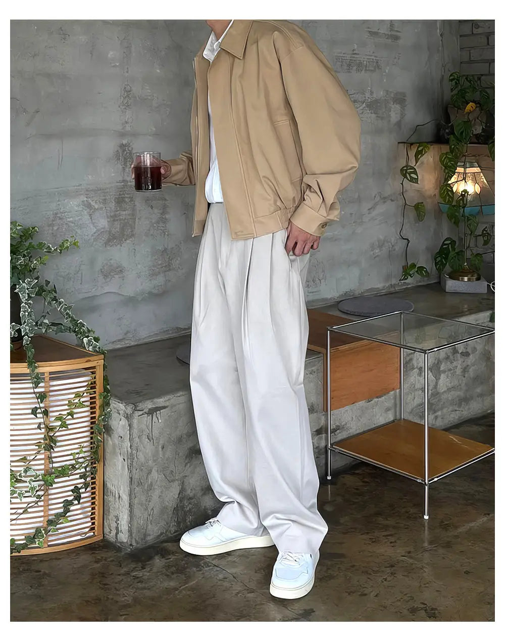 Chaqueta bomber beige de ajuste relajado con detalles de costura sutiles, combinada con pantalones de vestir anchos plisados color gris oscuro para hombre.