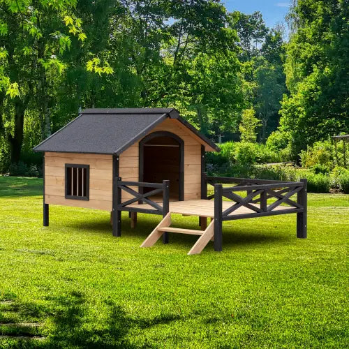 Une grande niche en bois pour chien avec porche, dotée d’un toit gris foncé, de rambardes noires et de marches, installée sur une pelouse.