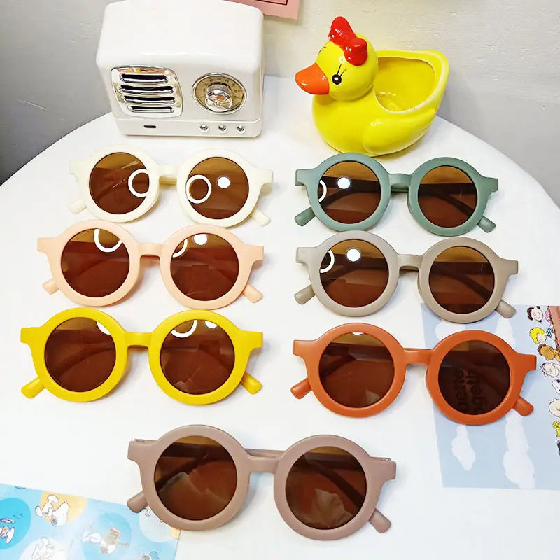 Un ensemble de lunettes de soleil rétro rondes pour chiens colorées pour enfants, dotées de verres marron et de montures pastel en blanc, beige, jaune, orange et vert, incluant une option de monture orange.