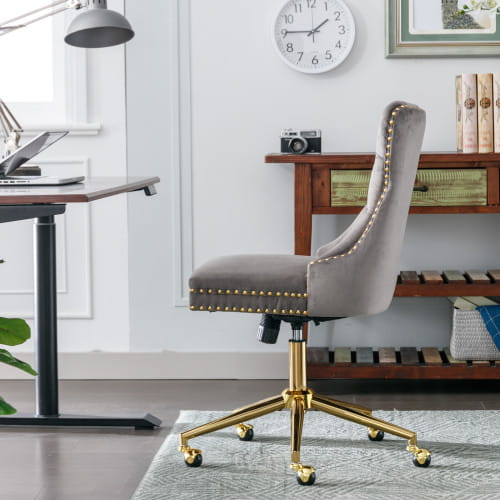 Chaise de bureau en velours gris avec dossier capitonné, piètement pivotant en métal à finition ton sur ton or et garniture à clous décoratifs, conçue pour un espace de travail professionnel.