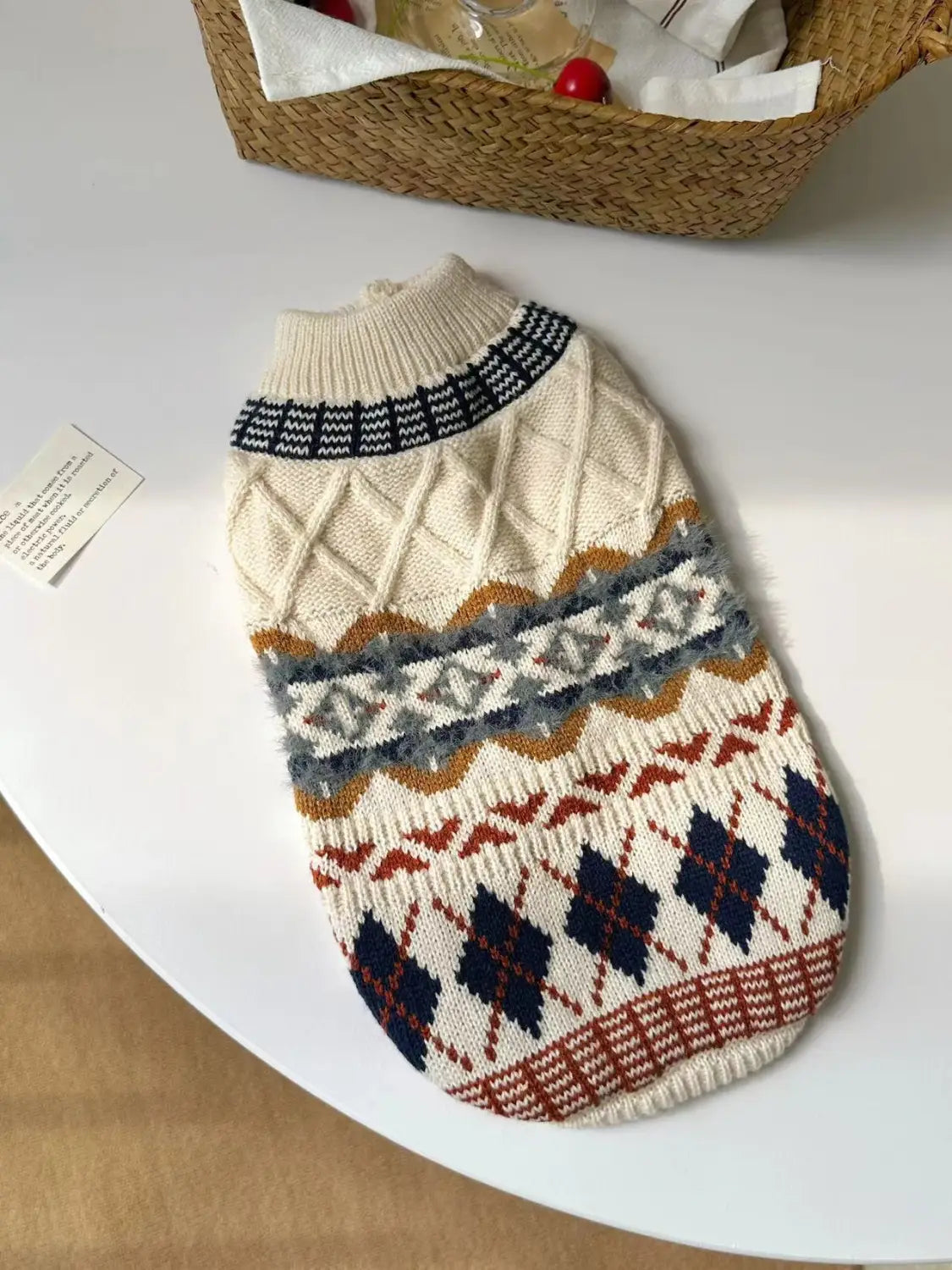 Pull pour chien tricoté couleur crème, présentant des motifs géométriques vintage complexes dans des tons marine, rouille et gris, conçu comme vêtement pour animal de compagnie.