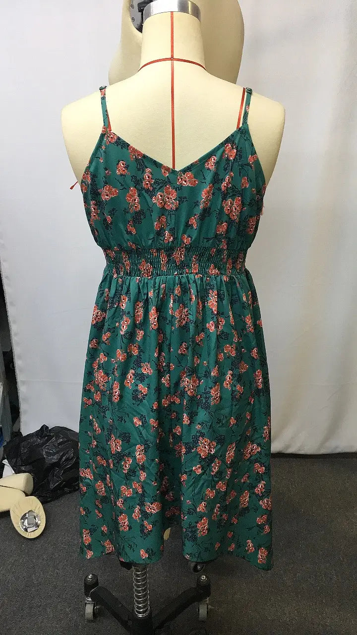 Ein grünes florales Retro-V-Ausschnitt-gesmoktes Mini-Sommerkleid mit dünnen Trägern, auf einem Schaufensterpüppchen präsentiert.