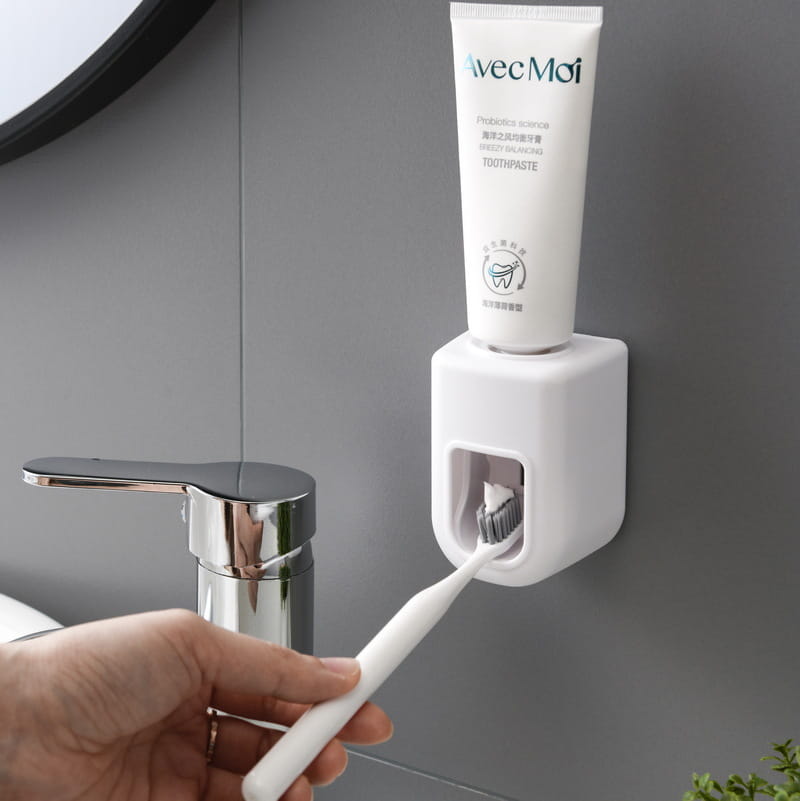 White plastic automatic toothpaste dispenser wall mount squeezer with a sleek modern design holding an Avecmoï toothpaste tube.