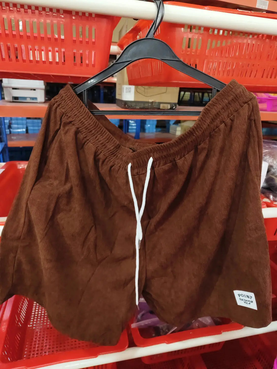 Shorts en velours côtelé marron à cordon de serrage pour hommes, avec un cordon de serrage blanc et une petite étiquette de marque « point » sur la partie inférieure droite de la jambe, conçus pour un usage sportif.