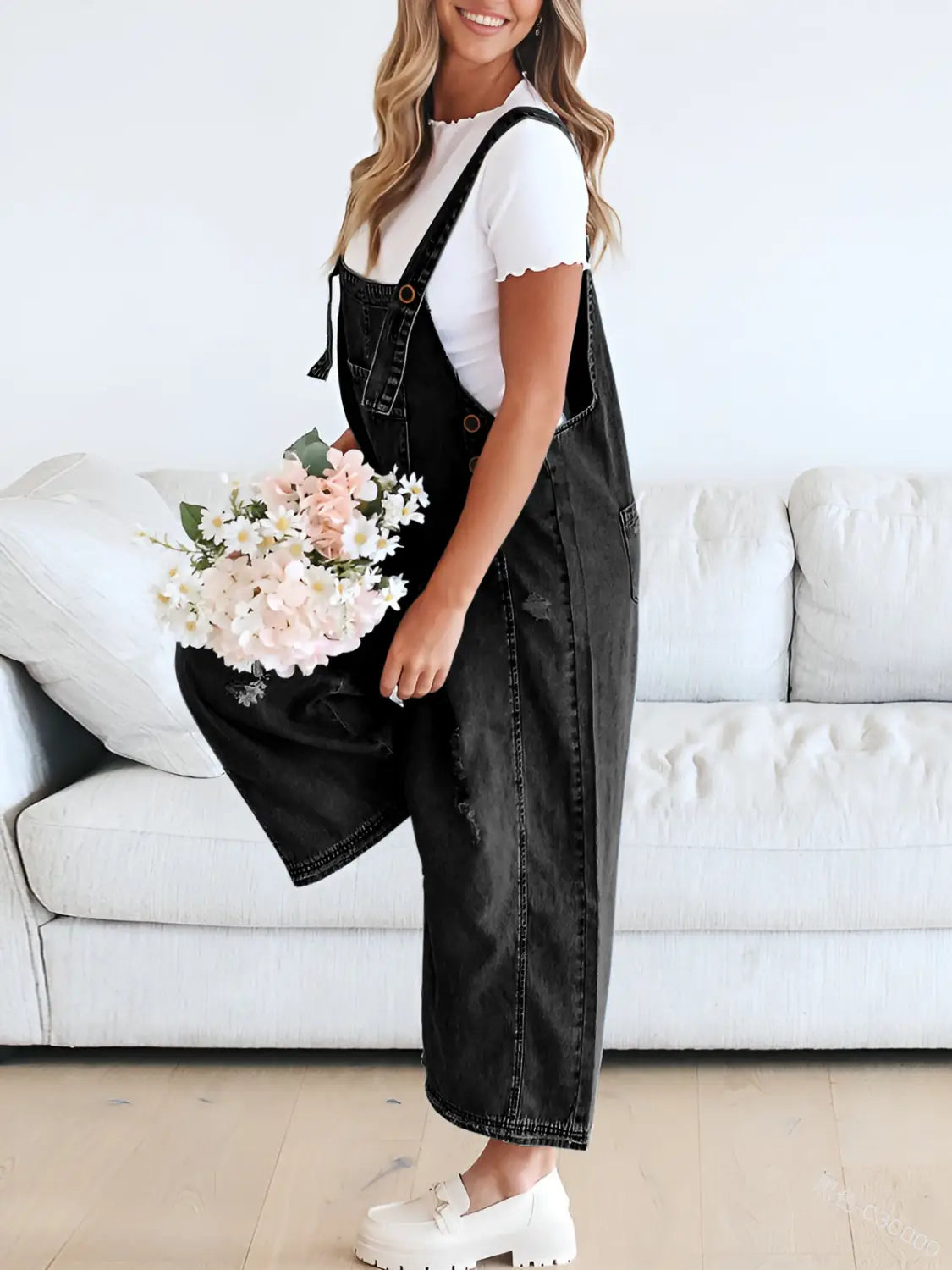 Women’s distressed black denim overalls with a relaxed wide-leg cut and adjustable straps displaying subtle distressing details.