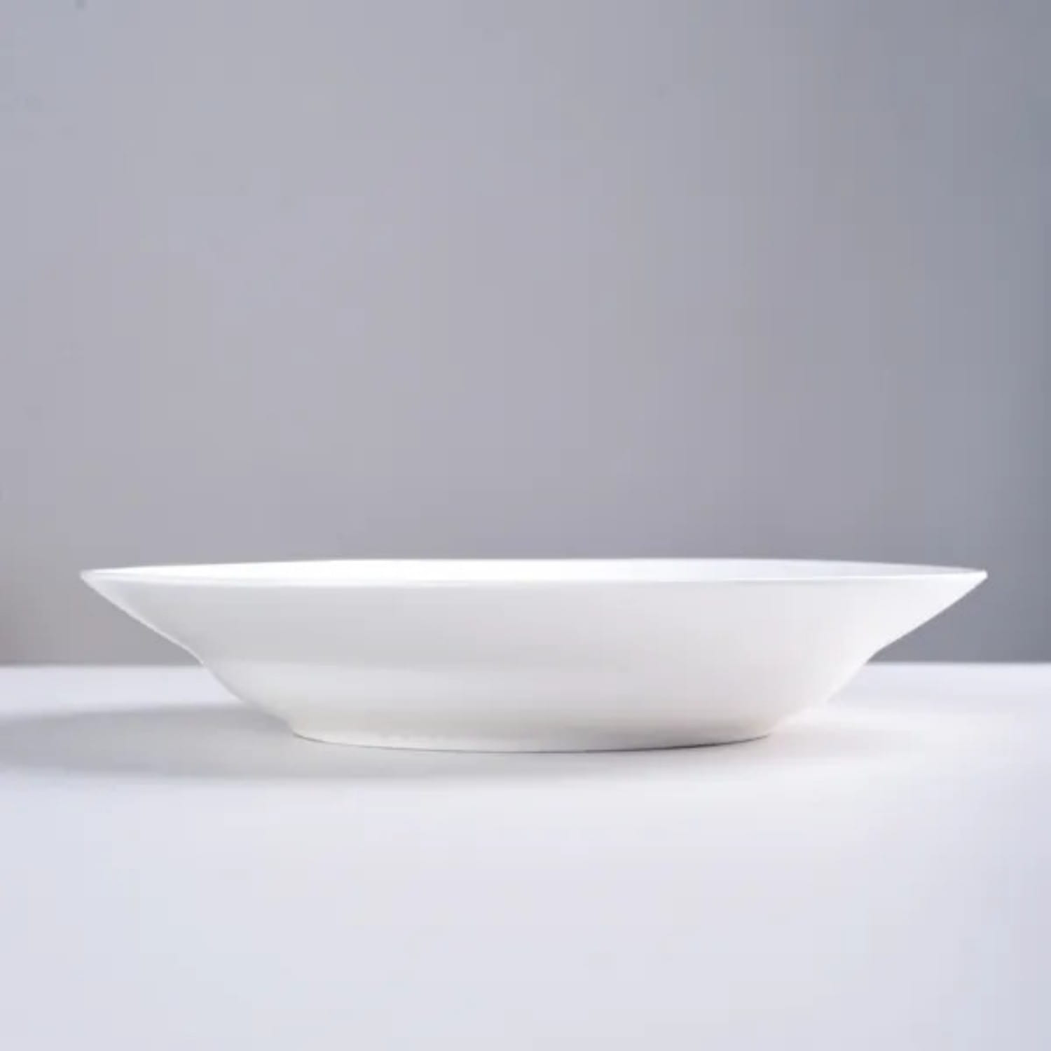 A minimalist white ceramic dinner plate with a smooth glossy finish and slightly flared rim from a set of six 9.5 inch bowls.