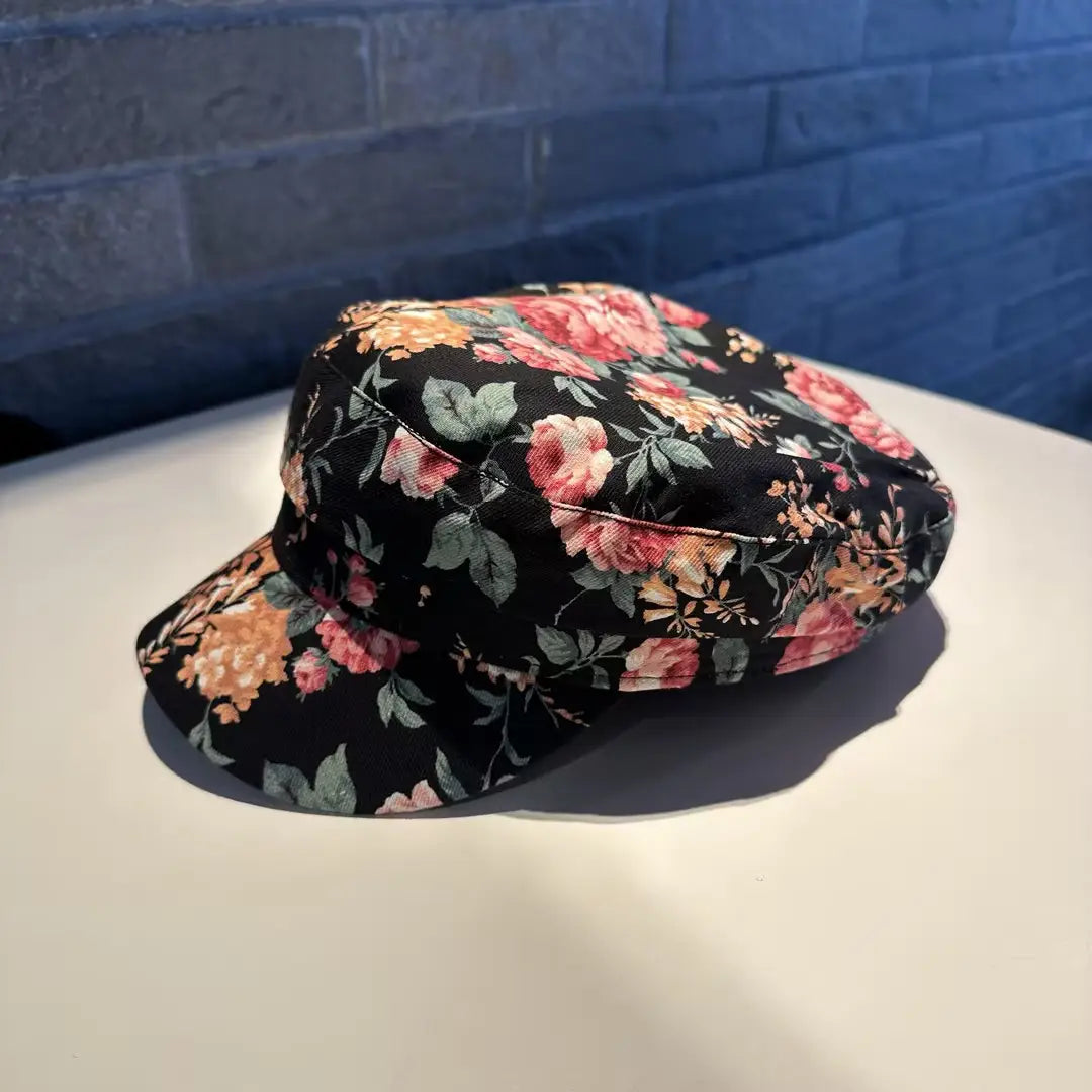 Gorra plana negra con patrón floral, con flores rosa y melocotón sobre una base de tela oscura; gorra tipo bucket hat floral, estilo coreano, impresa.