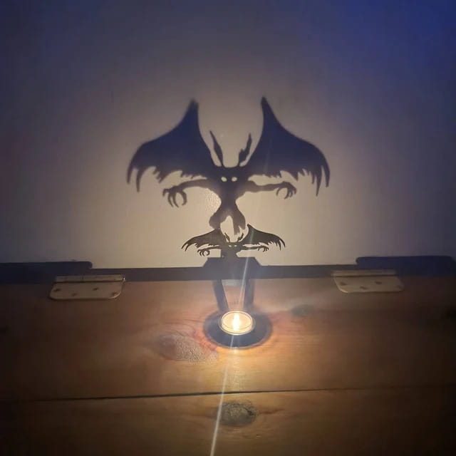 a black metal halloween bat candle holder casting a dragon shadow from a small candle on a wooden surface