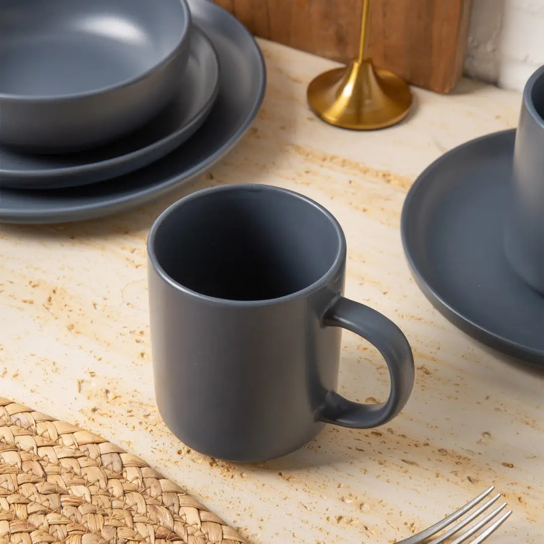 A matte gray ceramic mug with a simple modern design and matching handle from a 12-piece stoneware dinnerware set with matte glaze service for 3.