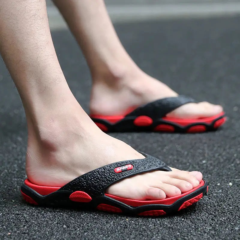 Men’s black and red rubber non-slip beach flip flops with textured straps and circular grip patterns on the sole designed for cushioned comfort.