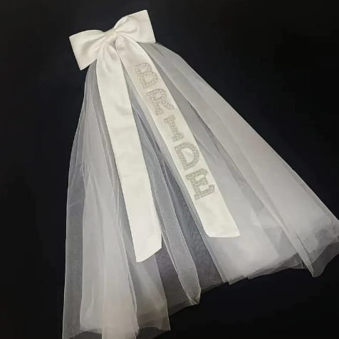 A delicate white tulle bridal bow veil adorned with a satin ribbon bow and sparkling rhinestone bride lettering.