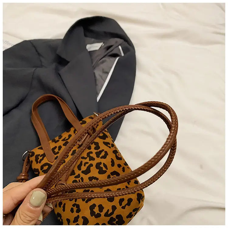 A tan and black leopard print suede mini bucket crossbody bag with braided brown leather handles.