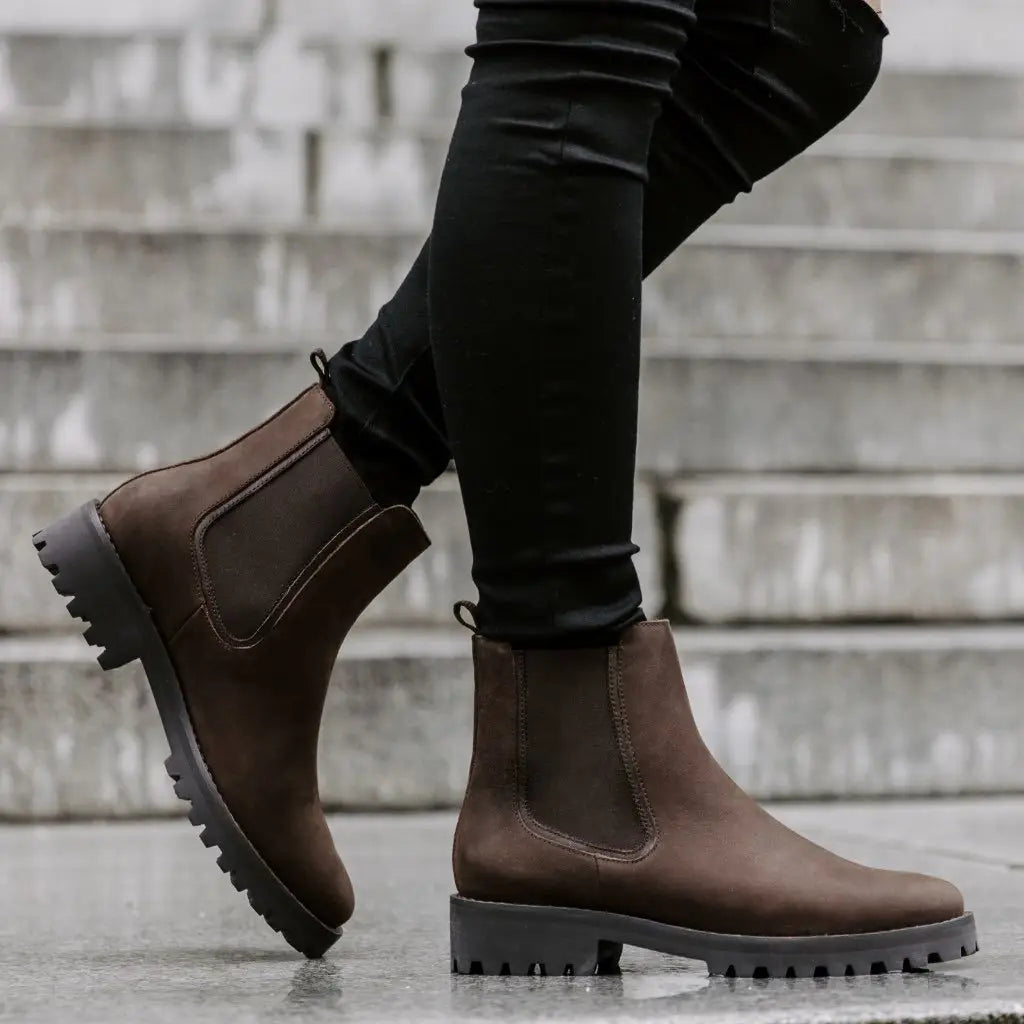 Brown suede Chelsea boots with a chunky black rubber platform sole shown from the back side.