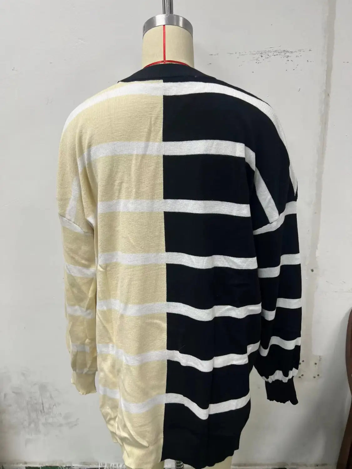 A long-sleeved knit cardigan featuring an oversized split color design with cream and black sections and horizontal white stripes, part of the women’s oversized split color striped knit sweater collection.