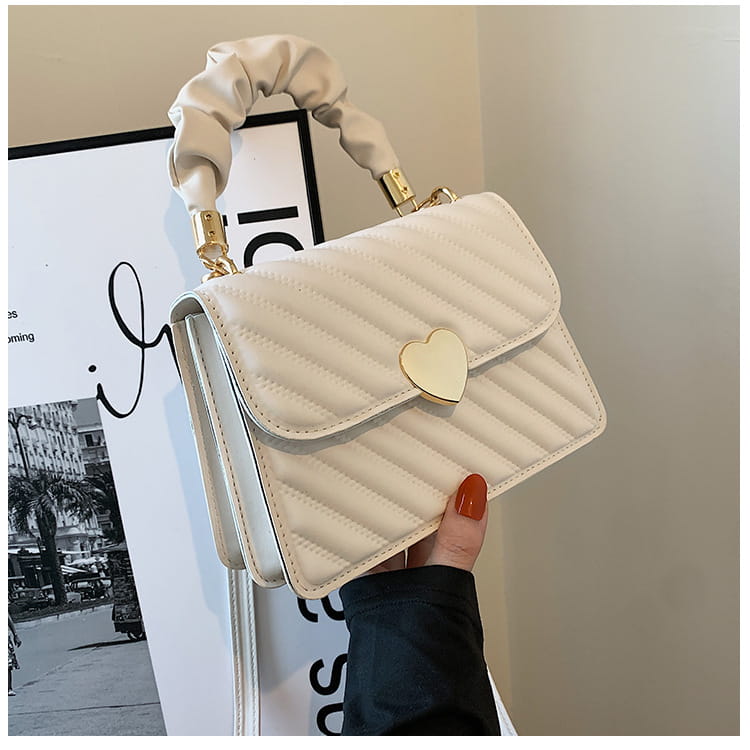 Cream-colored quilted crossbody bag with ruched top handle and gold-tone heart-shaped clasp.