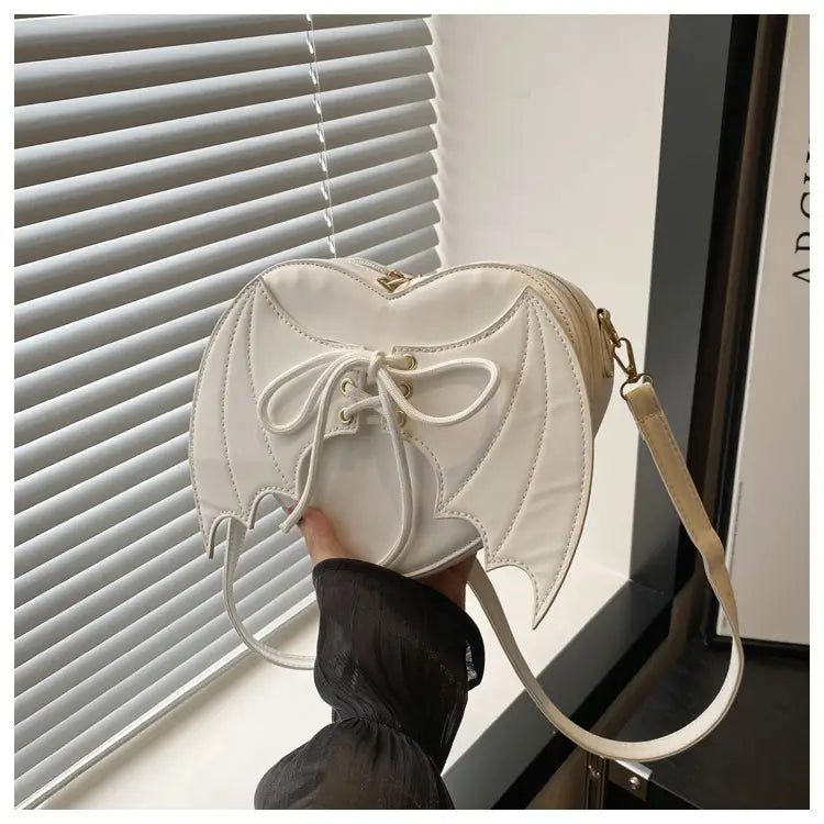 A white bat wing heart crossbody bag with lace up detailing and a gold tone clasp.
