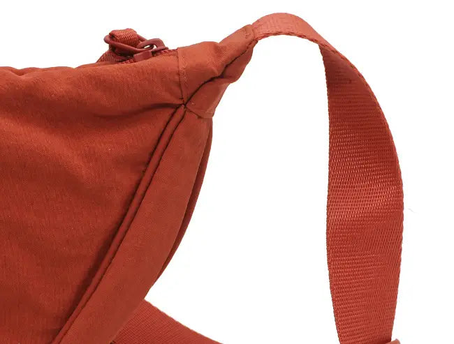 A rust-colored canvas nylon dumpling messenger bag with a curved adjustable crossbody strap and zipper closure.