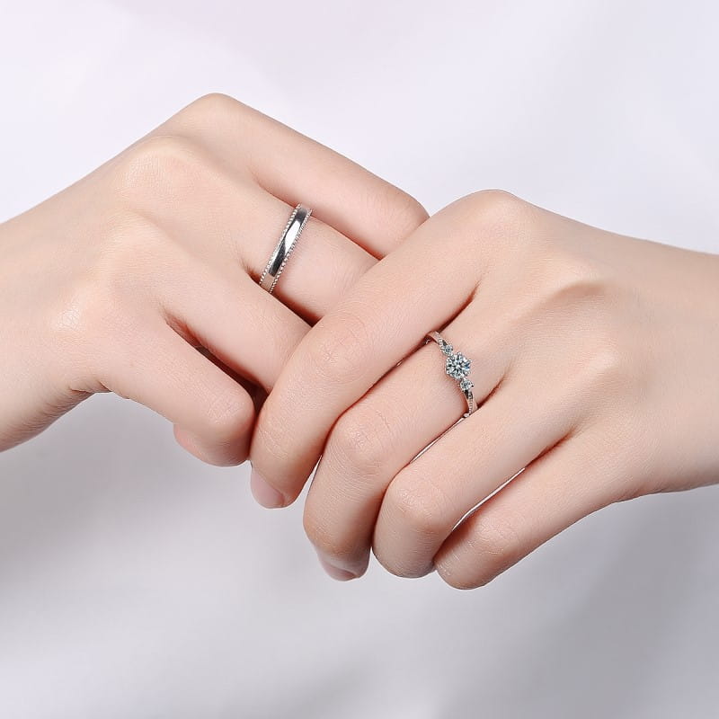 A pair of elegant sterling silver couple rings from Love at First Sight featuring a sleek band with embedded stones and a delicate floral design adorned with sparkling diamonds.