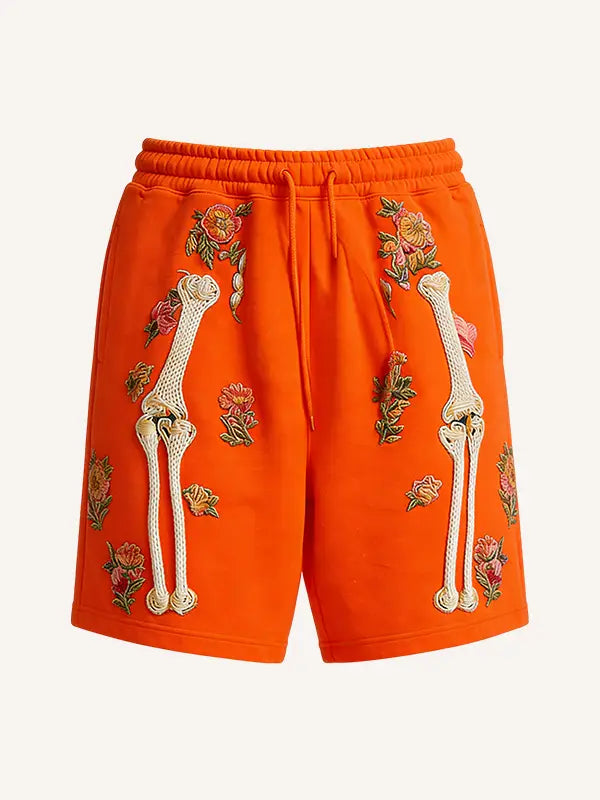 Vibrant orange polyester sweat shorts featuring embroidered white bone and floral patterns designed for men.