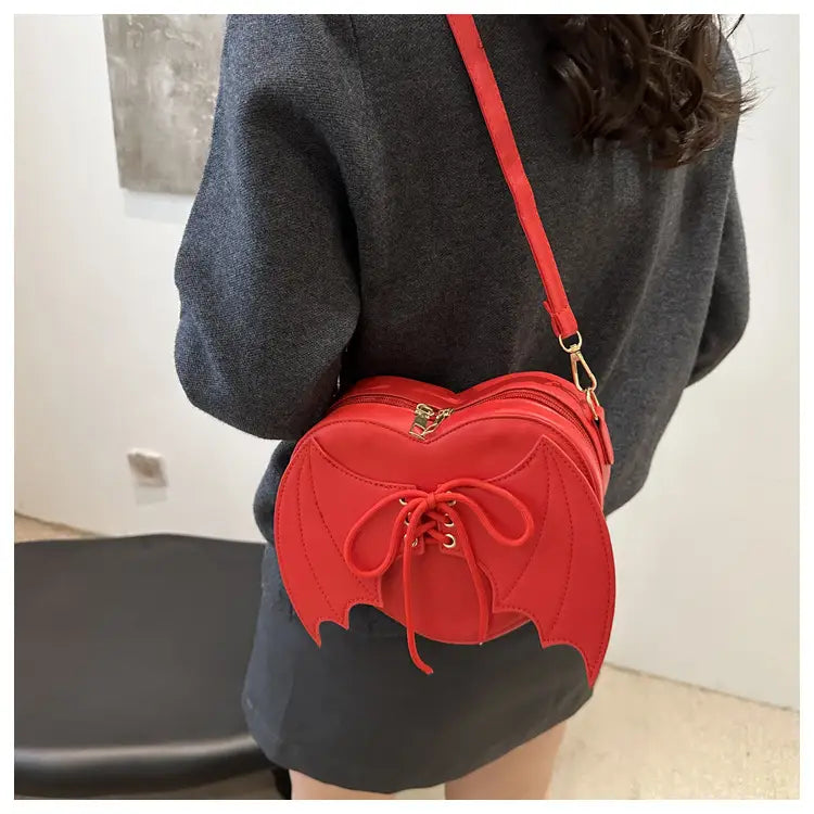 Red bat wing heart crossbody bag features a lace up front and gold tone hardware with a bat shaped silhouette.