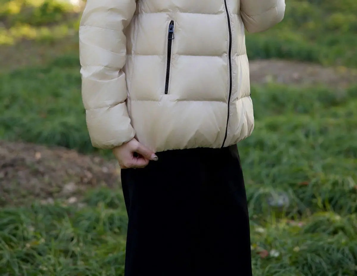 Cremefarbene kurze Steppjacke aus Daunen für Damen mit schwarzen Reißverschlussakzenten, ausgelegt als Winter-Puffer.