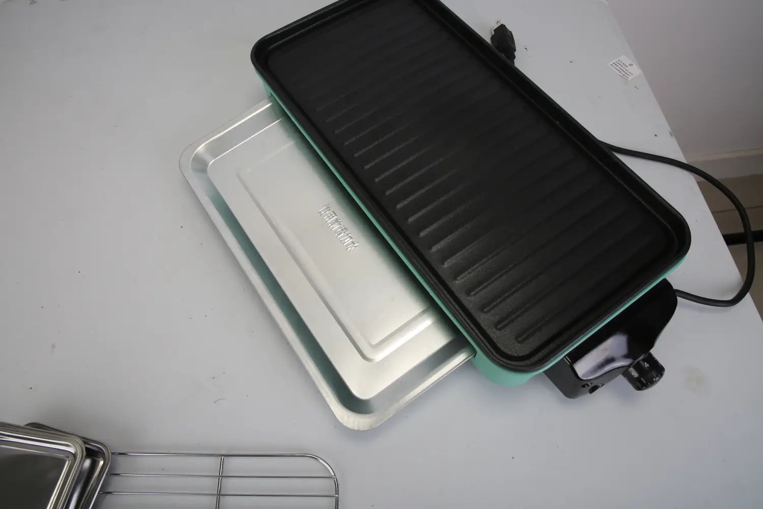 Gril électrique intérieur de 2000 W de couleur bleu-vert et noir, doté d’une surface de cuisson cannelée et de 3 bacs à raclette pour une cuisson intérieure polyvalente.
