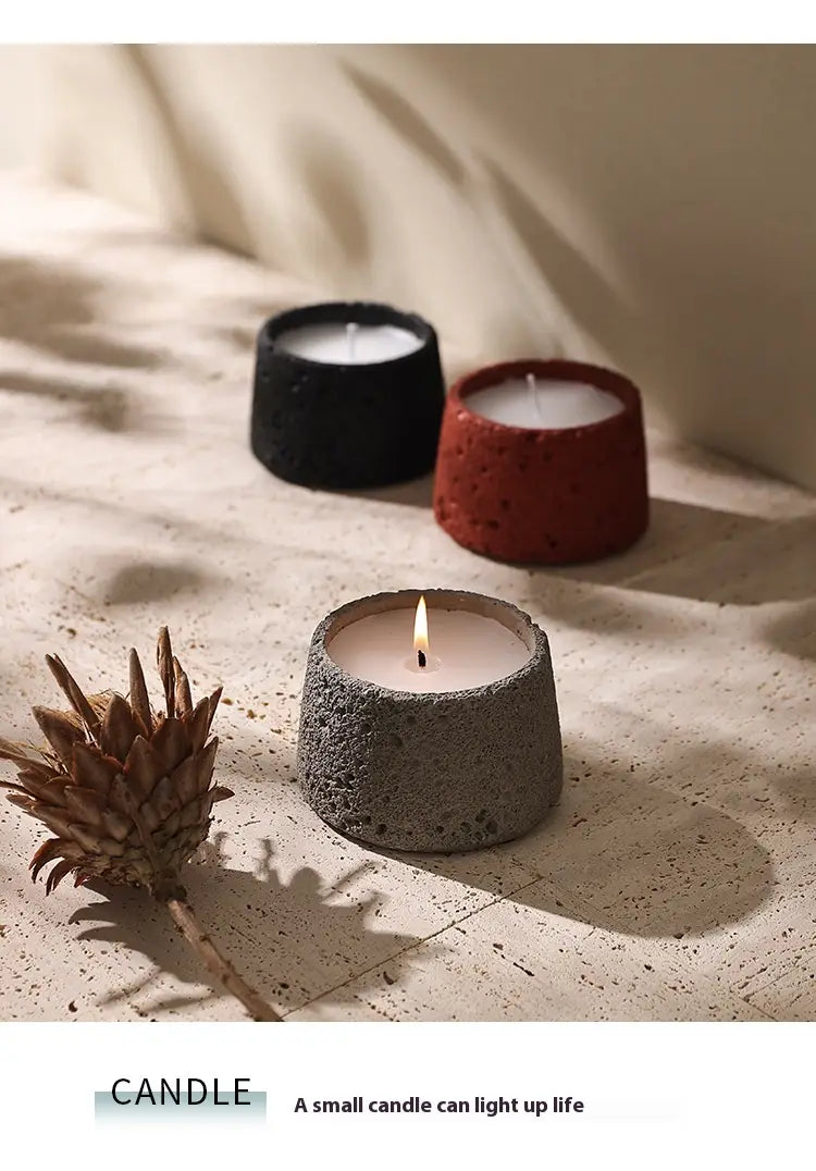 Support de bougie en ciment gris à texture en béton moucheté, coupelle d’aromathérapie en béton moucheté, avec une bougie en cire blanche allumée à l’intérieur.