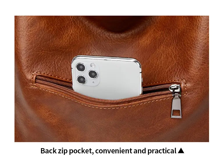 Eine braune Vintage-Leder-Totebag mit hinterer Reißverschlusstasche, in der ein weißes Smartphone verstaut ist; von der Rückseite gezeigt.