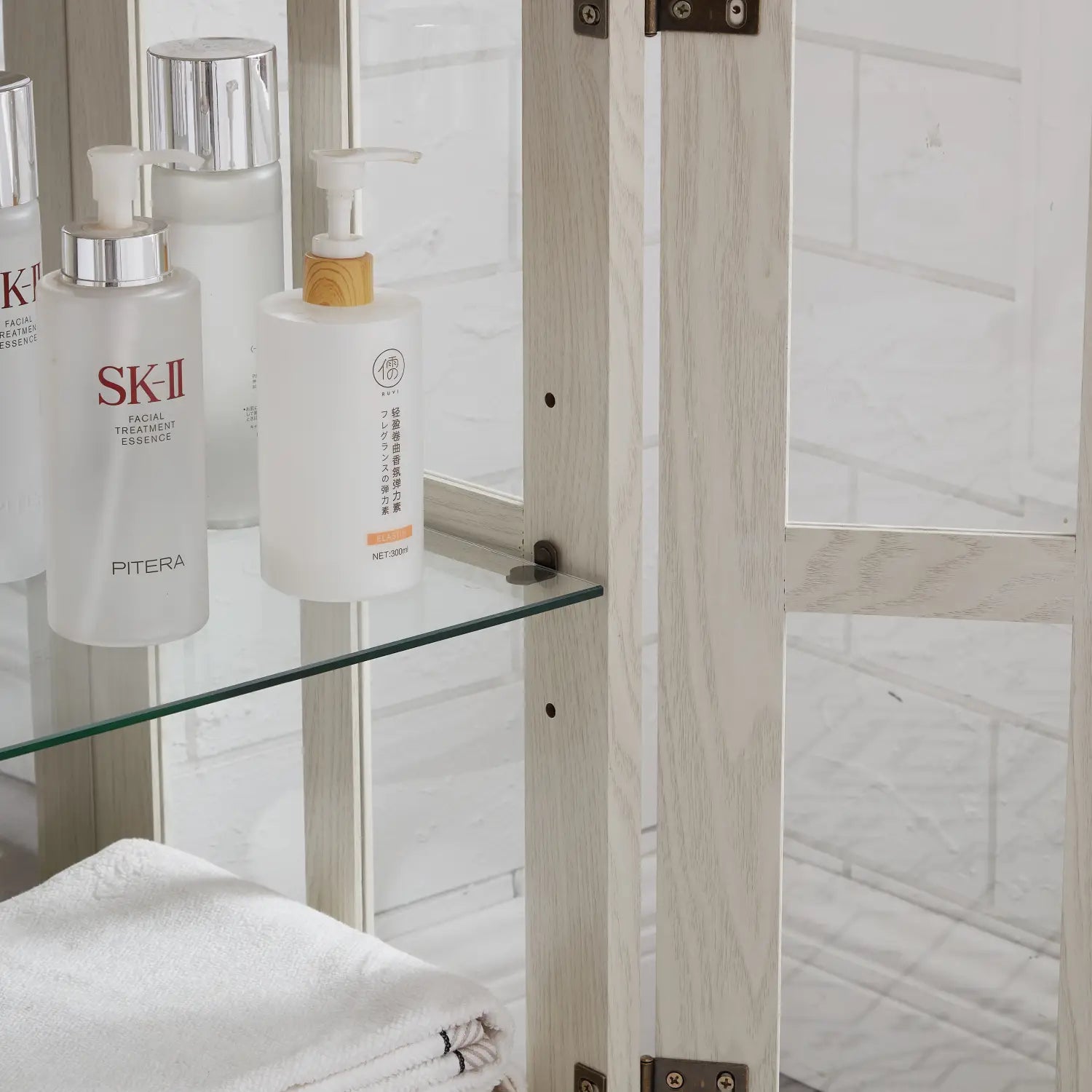 led curio display cabinet with lattice doors in white shown alongside a white sk-ii facial treatment essence bottle with a silver pump and frosted glass body