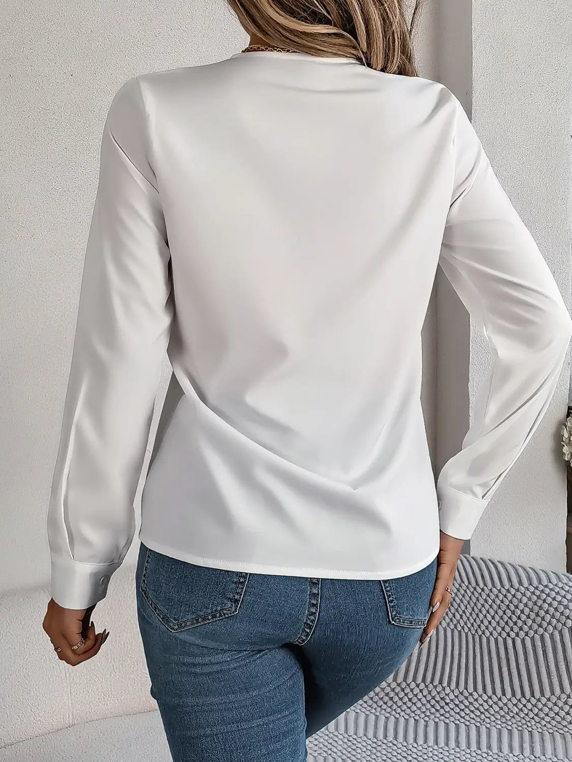 A sleek white satin v neck wrap blouse with long sleeves black trim and smooth flowing fabric.