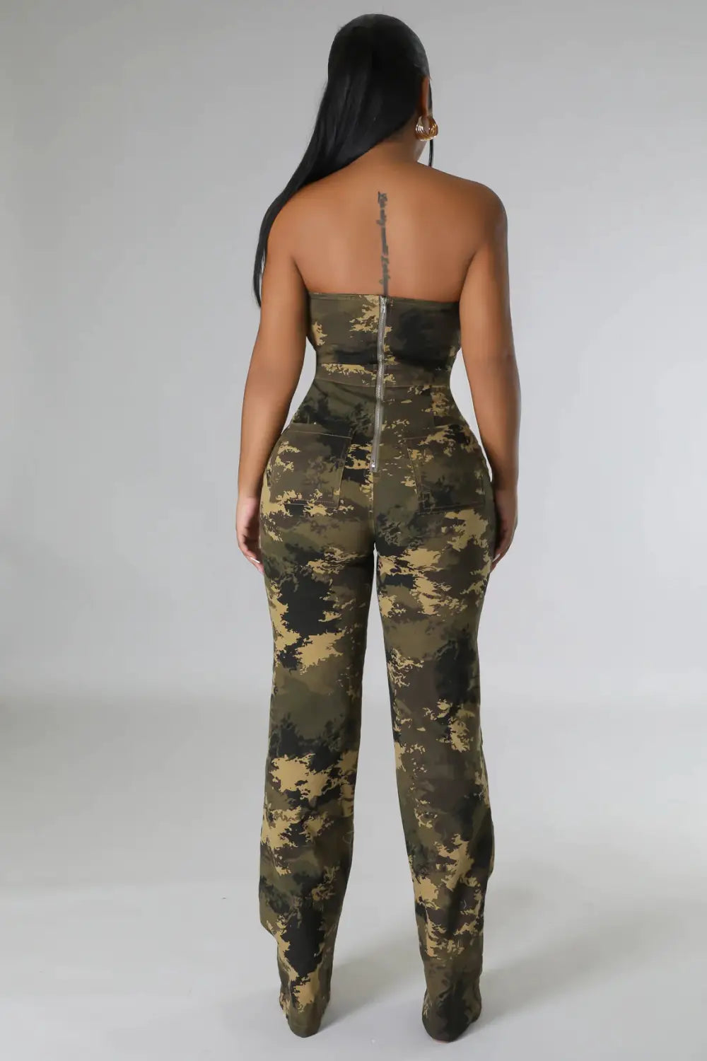 Eine Frau trägt in einer Produktabbildung einen Camouflage-Aussteller-Jeansjumpsuit mit eng anliegendem trägerlosem Jumpsuit mit Oliven- und Tan-Camouflage-Muster.