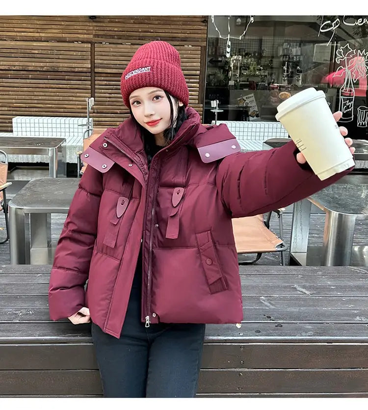 Veste courte matelassée à capuche pour femme bordeaux, avec panneaux matelassés, col haut et patchs de tissu assortis sur les épaules, conçue pour l’habillement d’hiver chaud.