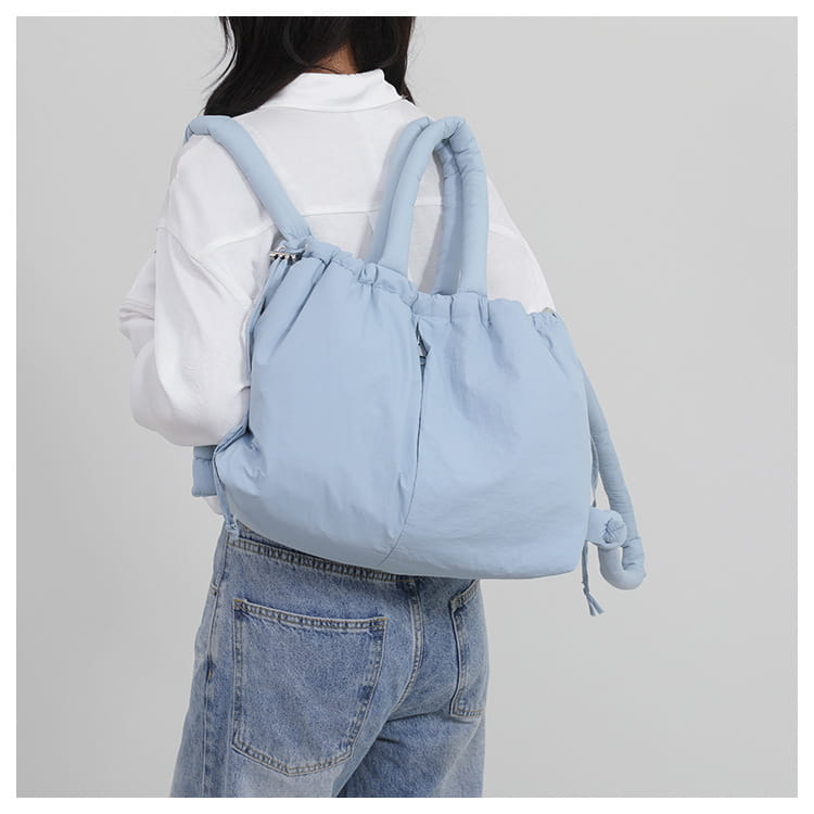 Light blue quilted puffer tote bag made of lightweight nylon featuring soft texture drawstring closure padded shoulder straps and a playful elephant-shaped tassel.