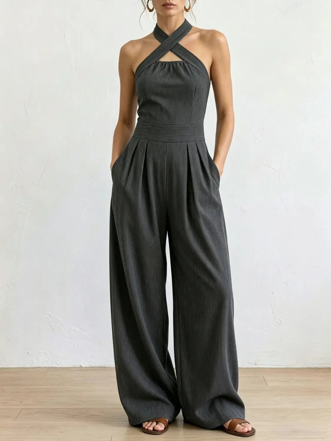 Ein eleganter dunkelgrauer Halterneck-Jumpsuit mit Kreuzrücken-Design und plissierten Hosen mit weitem Bein, von hinten dargestellt.