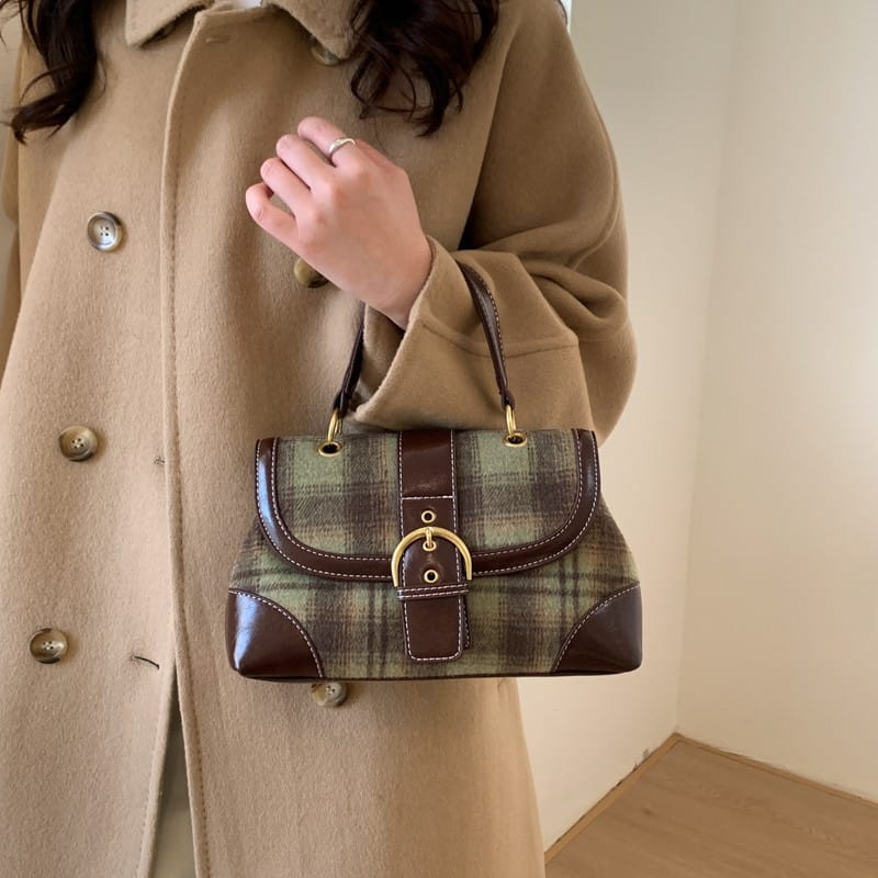 Bolso bandolera vintage de cuadros que presenta tela de cuadros marrón y verde con ribete de cuero, herrajes en tono dorado y cierre tipo solapa.