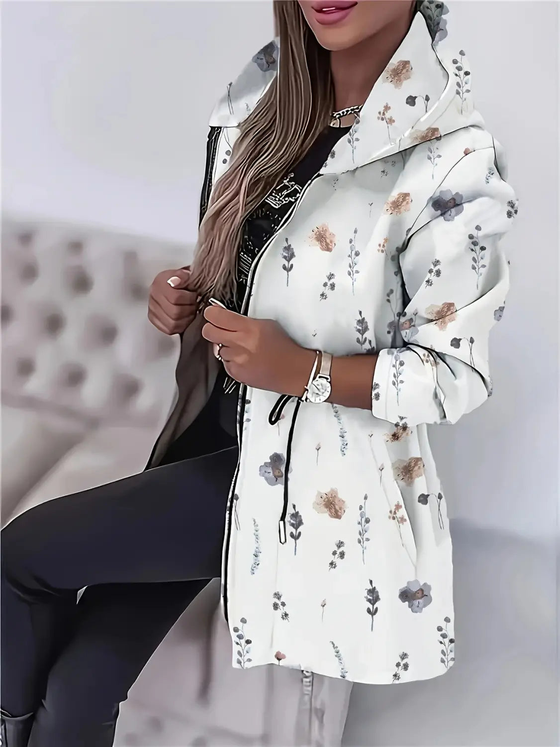 Veste à capuche zippée blanche à motifs floraux, avec fermeture éclair noire et cordon de serrage, comportant des détails floraux brodés.