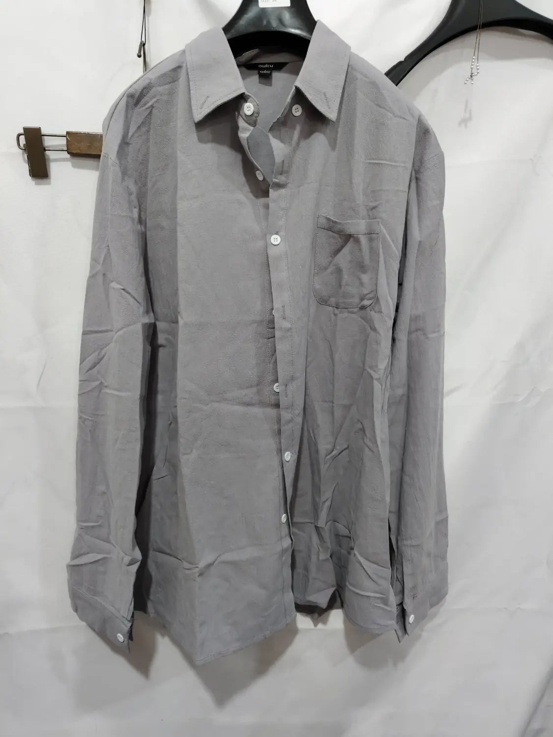 Chemise décontractée en coton et lin gris, à manches longues, avec col et poche poitrine, suspendue à un cintre noir.