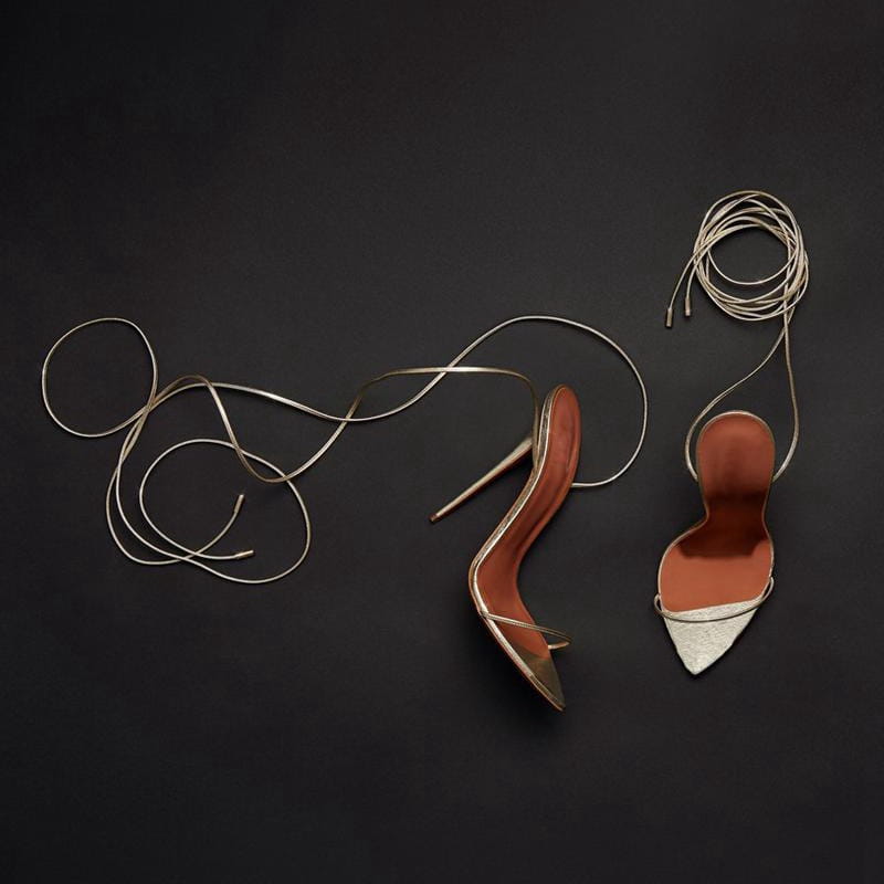A pair of elegant metallic gold stiletto sandals featuring slender ankle wrap straps and a pointed toe design.