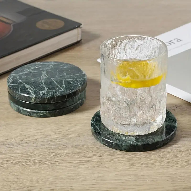 Green marble coasters set of 4 round stone pads with white veining featuring one coaster holding a textured glass tumbler filled with ice and lemon.
