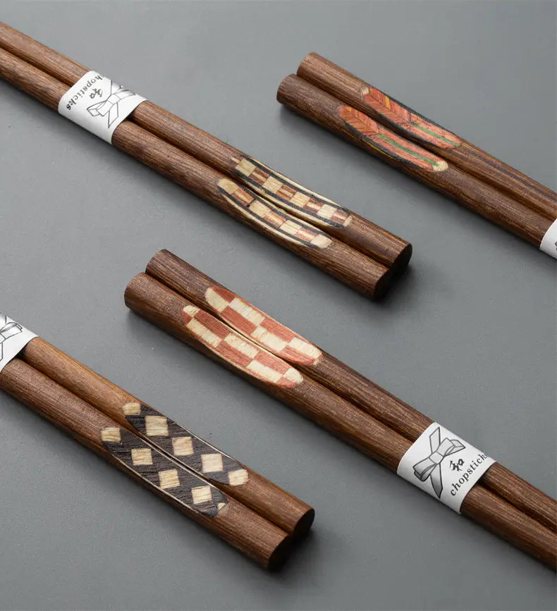 Set of ten pairs of wooden chopsticks with non slip tips featuring hand painted geometric and feather designs in natural wood tones each bundled with a white paper band with a bow illustration.