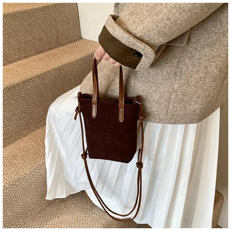 Brown suede mini bucket crossbody bag with matching leather handles and adjustable shoulder strap featuring a retro leopard print design.