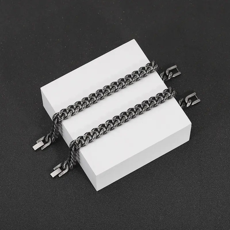 Two matte black stainless steel curb chain bracelets featuring silver-toned clasp mechanisms.