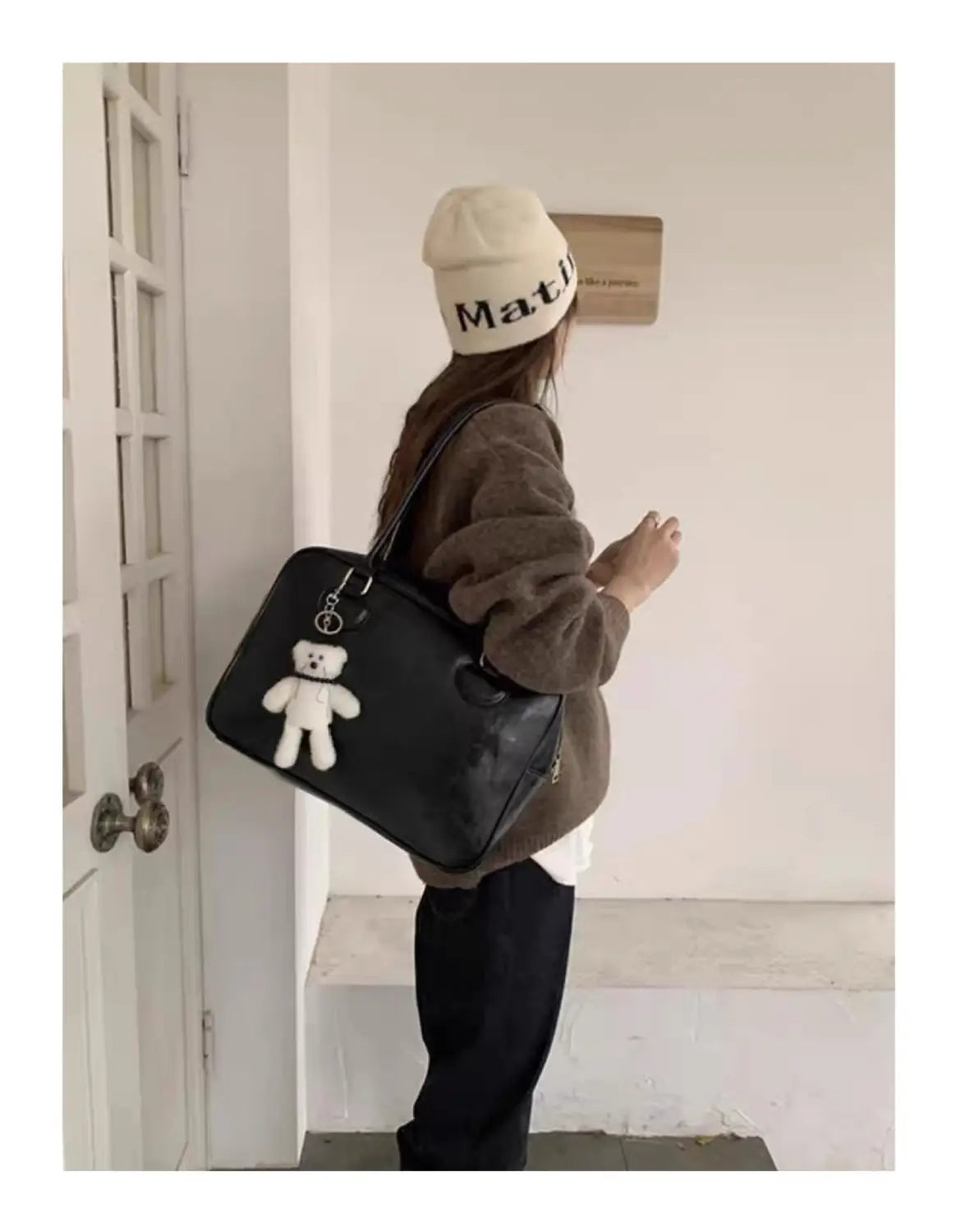 Black leather large capacity shoulder bag with a white teddy bear charm hanging from the strap.