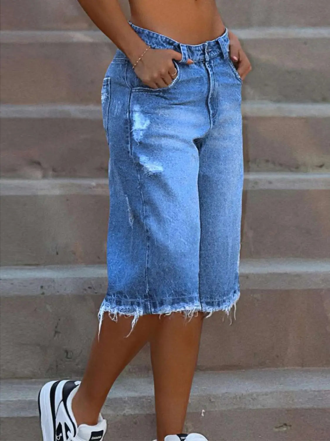 Pantalones capri de mezclilla azul claro con aspecto desgastado y desgarros, con dobladillos deshilachados y parches con desgaste.