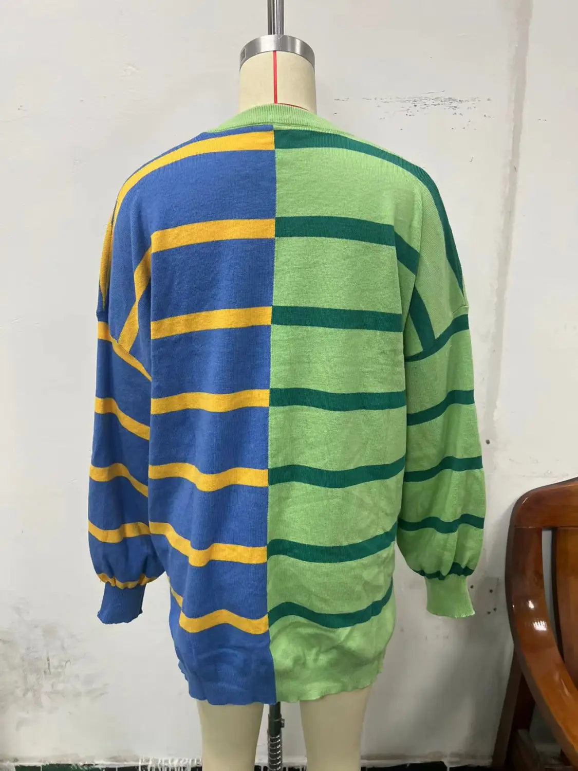 Women’s oversized split color striped knit sweater featuring vibrant blue and yellow horizontal stripes on one side and green and dark green stripes on the other.