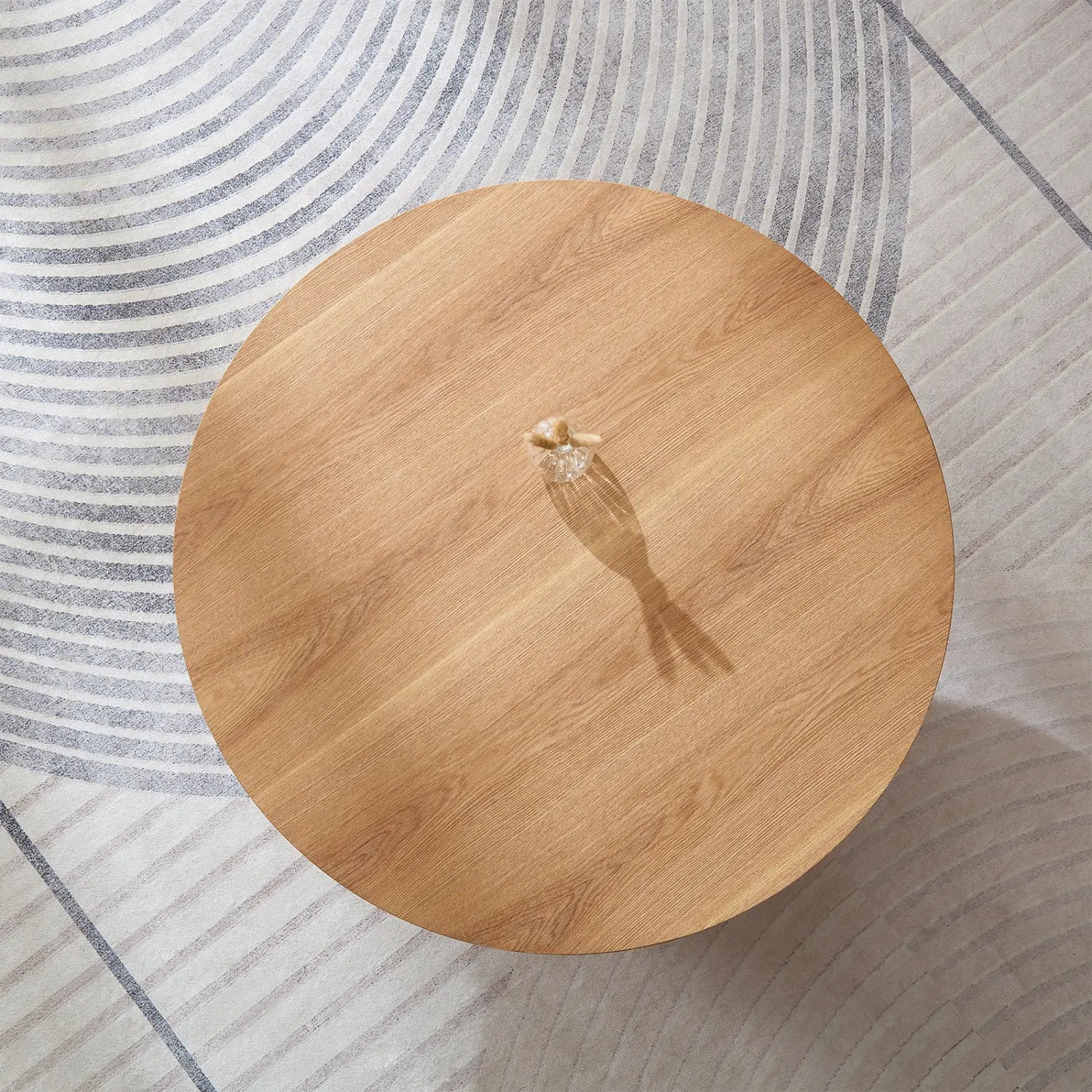 Mesa de centro redonda de madera con un acabado en tono marrón claro natural y vetas de madera visibles, con una base de pedestal moderna.