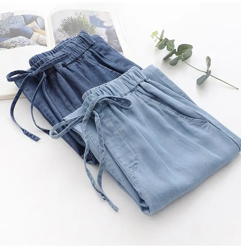 A pair of light blue high waisted harem jeans denim shorts with elastic waistbands and drawstrings.