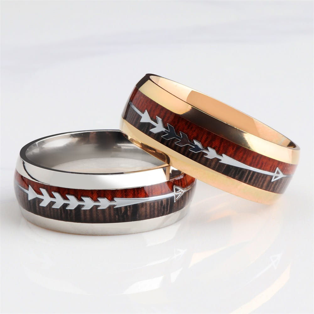 Two men’s wedding bands in rose gold and stainless steel featuring a central dark wood grain band with silver arrow inlays.