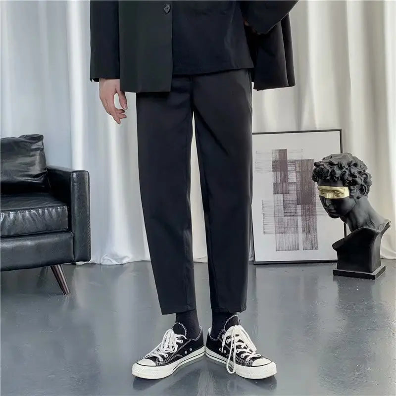 Herren-Modern-Slim-Fit-Geradeschneider-Schwarze Baumwollhosen mit dezentem Bügelfaltenwurf, kombiniert mit schwarzen Converse-Sneakers.