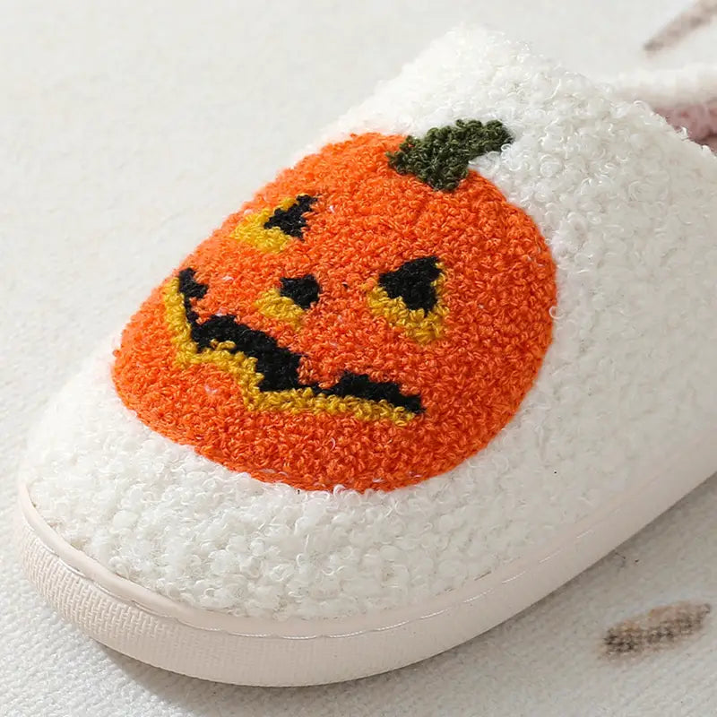 White plush Halloween slipper featuring a vibrant orange jack-o-lantern embroidered with black and yellow facial details on a fuzzy white material.